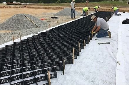 Cuadrilla estirando y fijando con estacas los paneles de geocelda sobre geotextil